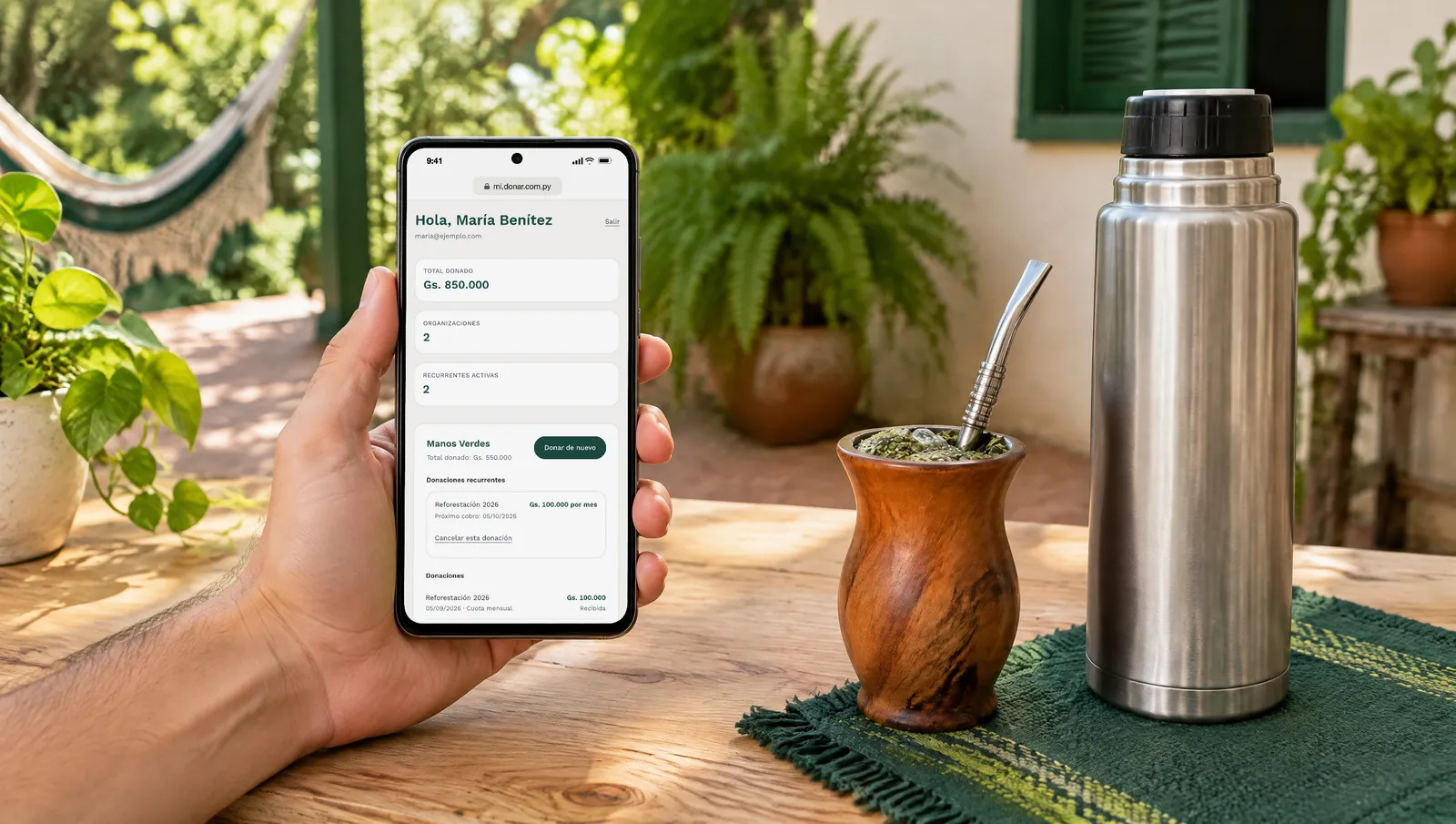 Una mano sostiene un celular con el portal del donante abierto: lo que donó, su donación mensual y el enlace para cancelarla, junto a un equipo de mate.